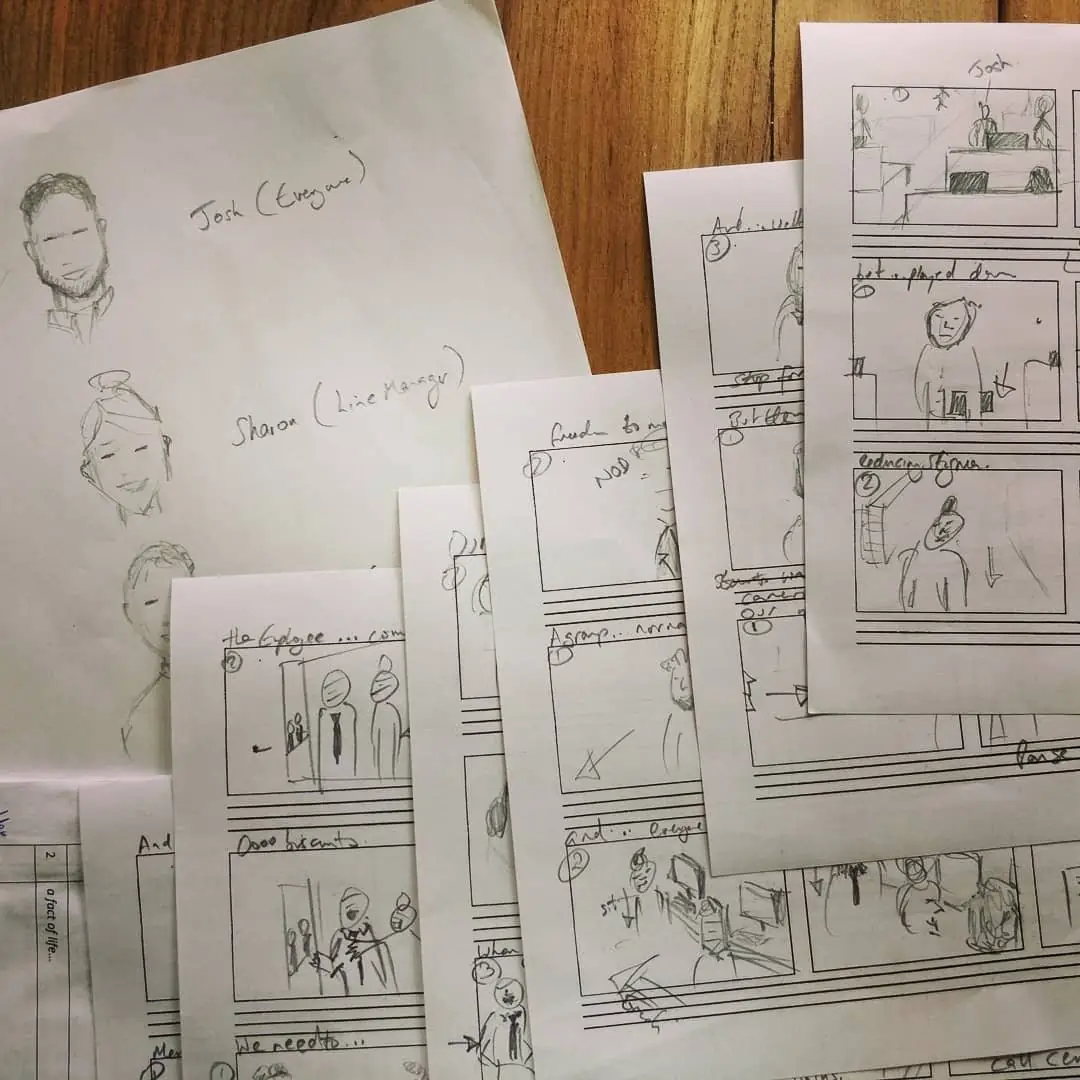 Hand-drawn storyboard sheets spread on a wooden table, with sketched faces and framed panels